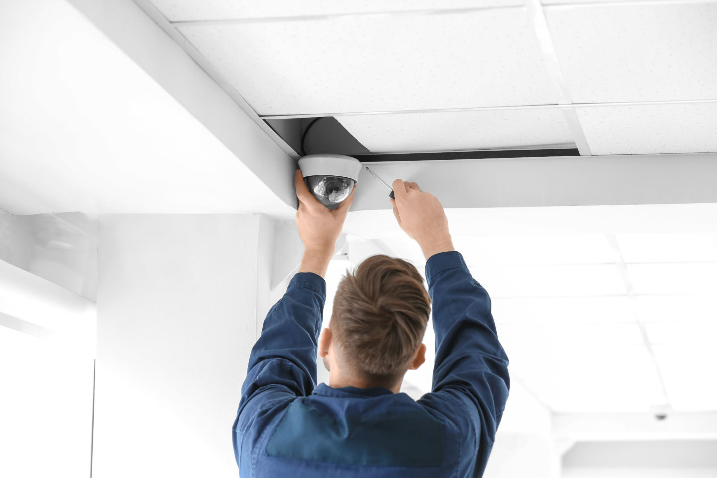Technician installing CCTV camera on ceiling indoors